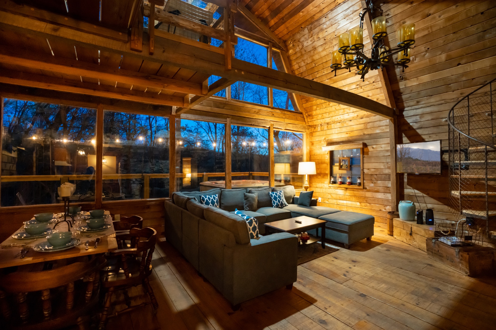 Rustic Retreat's vaulted living room at dusk, with a stone fireplace and a wrought iron chandelier